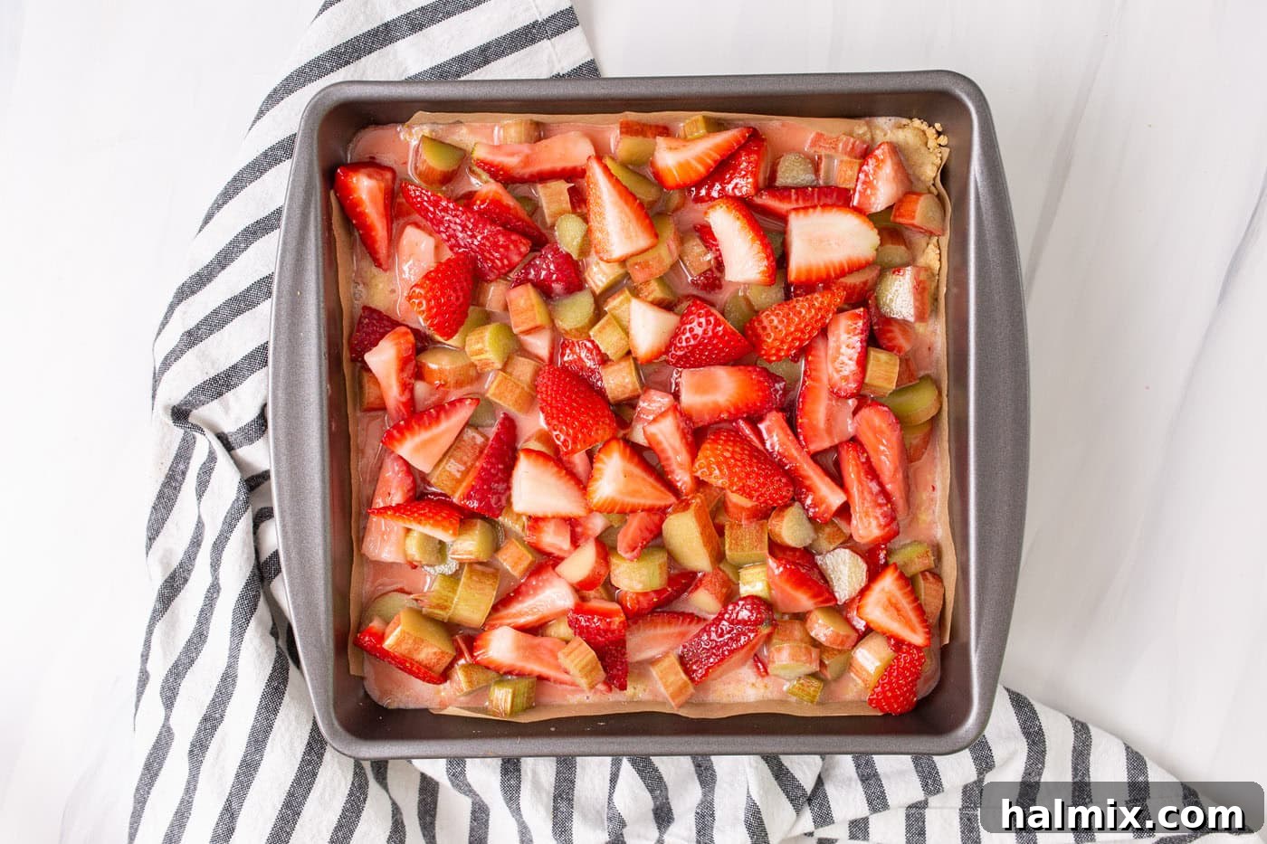 Fresh strawberries and rhubarb mixture generously spread over the crumble crust in a baking pan, creating a colorful layer