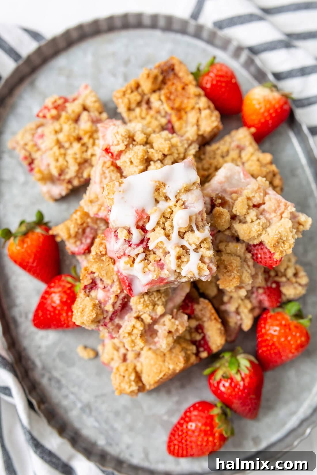 Strawberry Rhubarb Crumble Bars artfully piled on a beautiful white serving platter, garnished with a few fresh berries, ready for guests or a dessert table