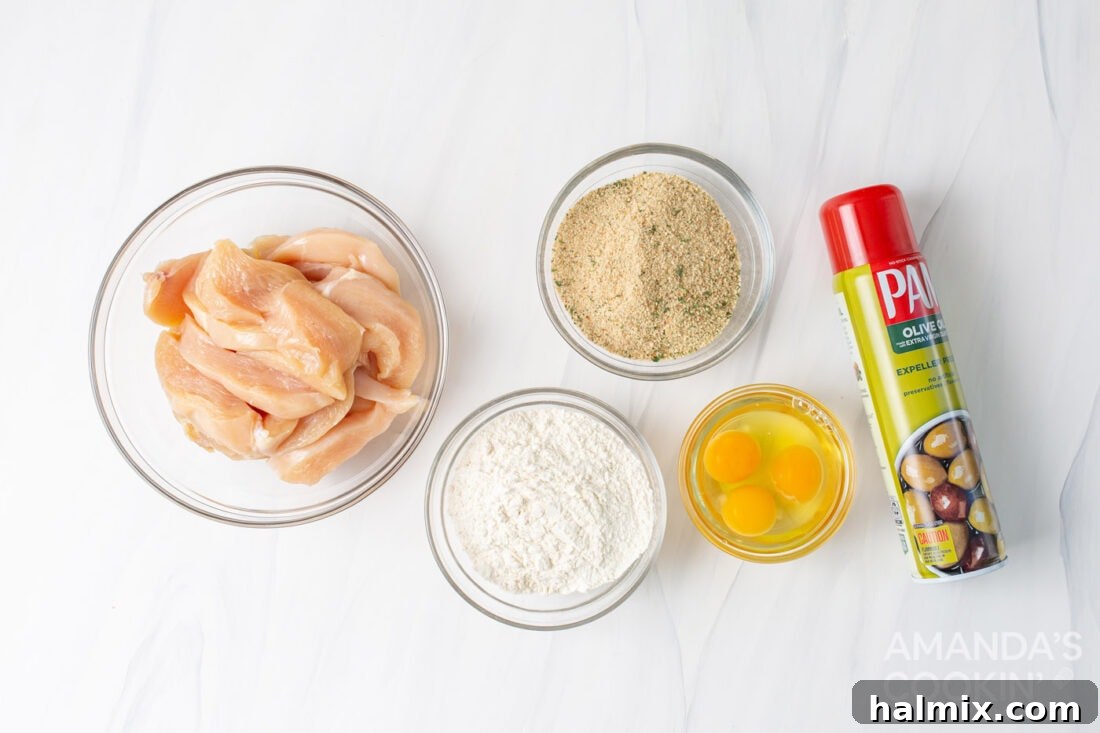 Bowls of flour, whisked eggs, and seasoned breadcrumbs, with raw chicken tenders ready for breading