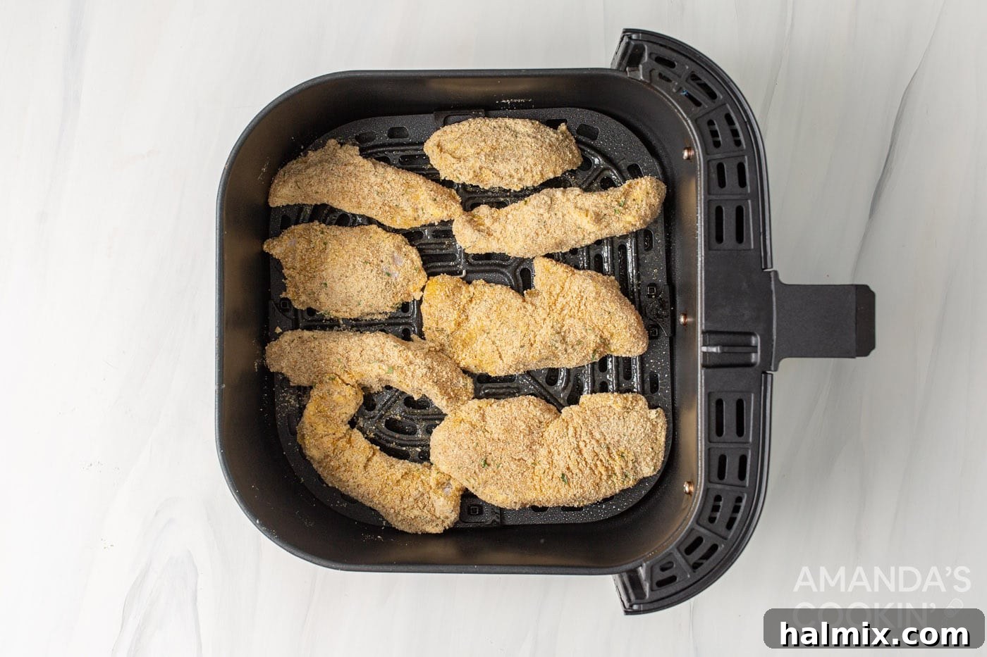 Breaded chicken tenders neatly arranged in a single layer within an air fryer basket, ready for cooking