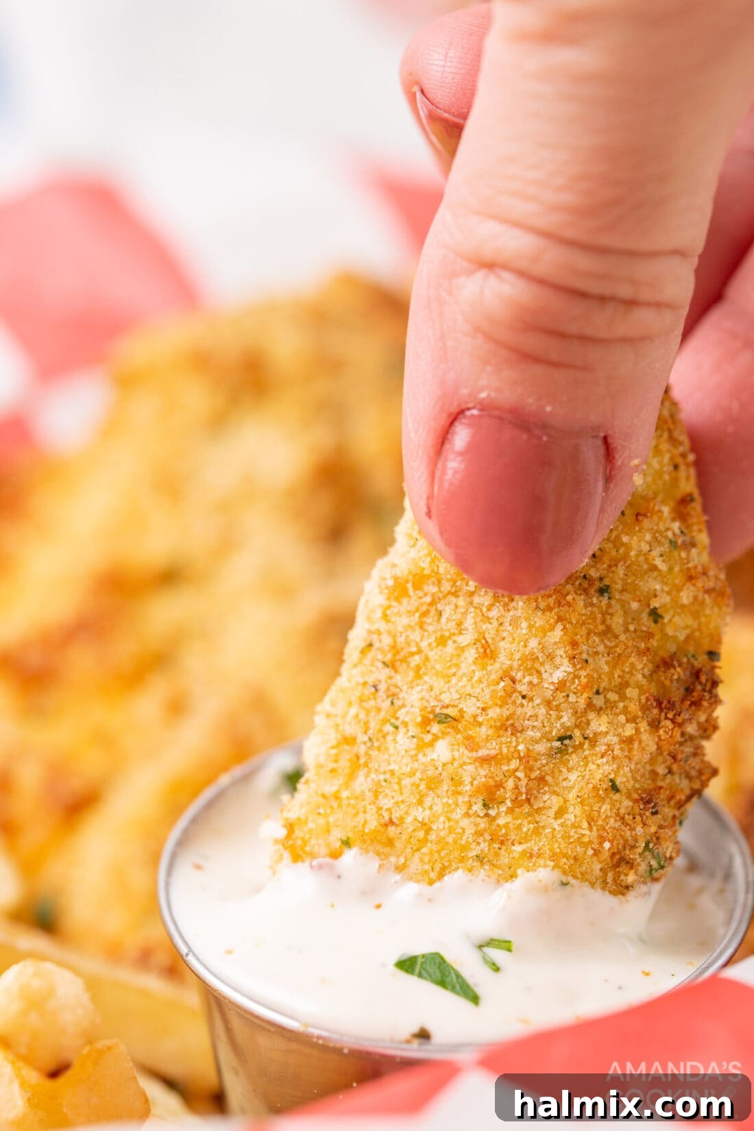 Hand dipping a golden air fryer chicken tender into a small bowl of creamy ranch dressing
