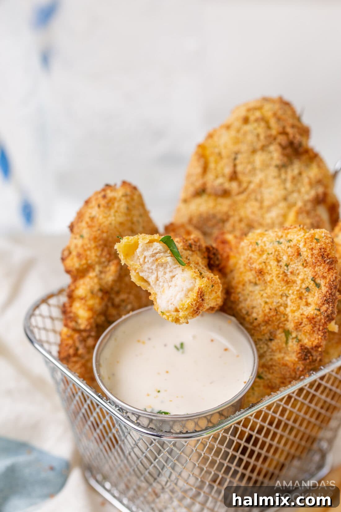 Air fryer chicken tenders served in a black air fryer basket with a small bowl of ranch dressing on the side