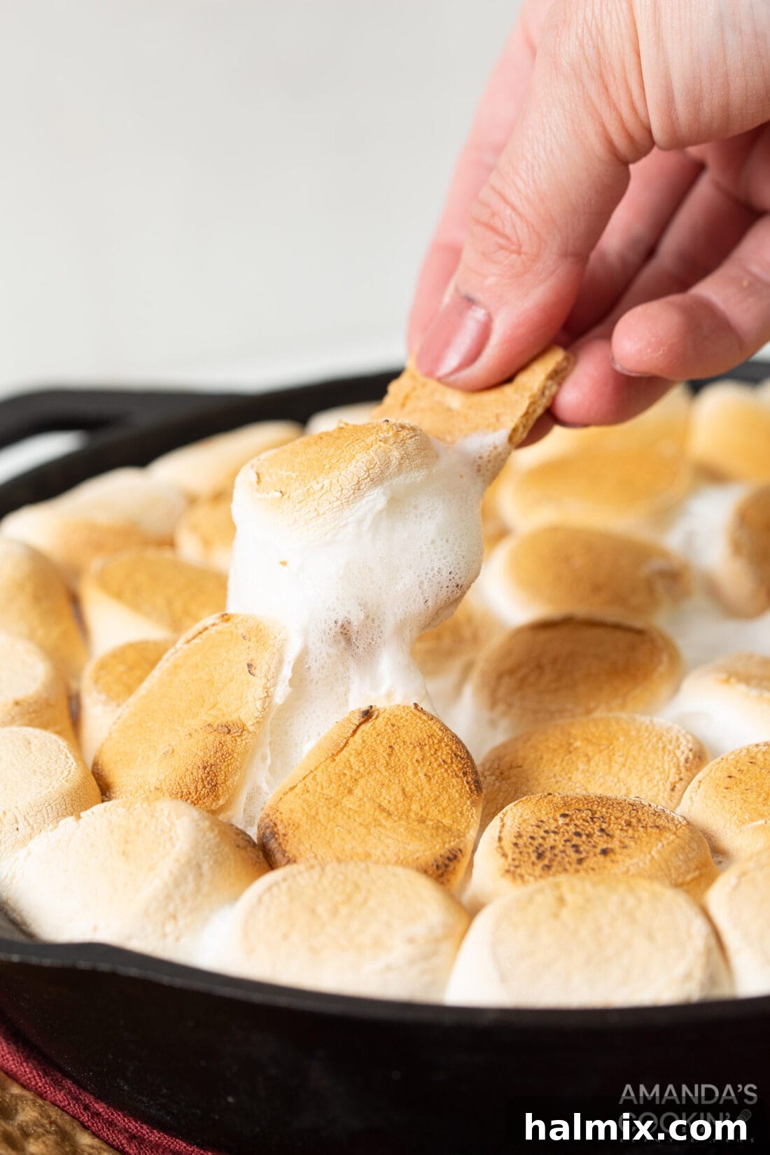 Gooey S'mores Skillet 3 Scoop of S'mores Dip on a graham cracker, showing gooey chocolate and toasted marshmallow