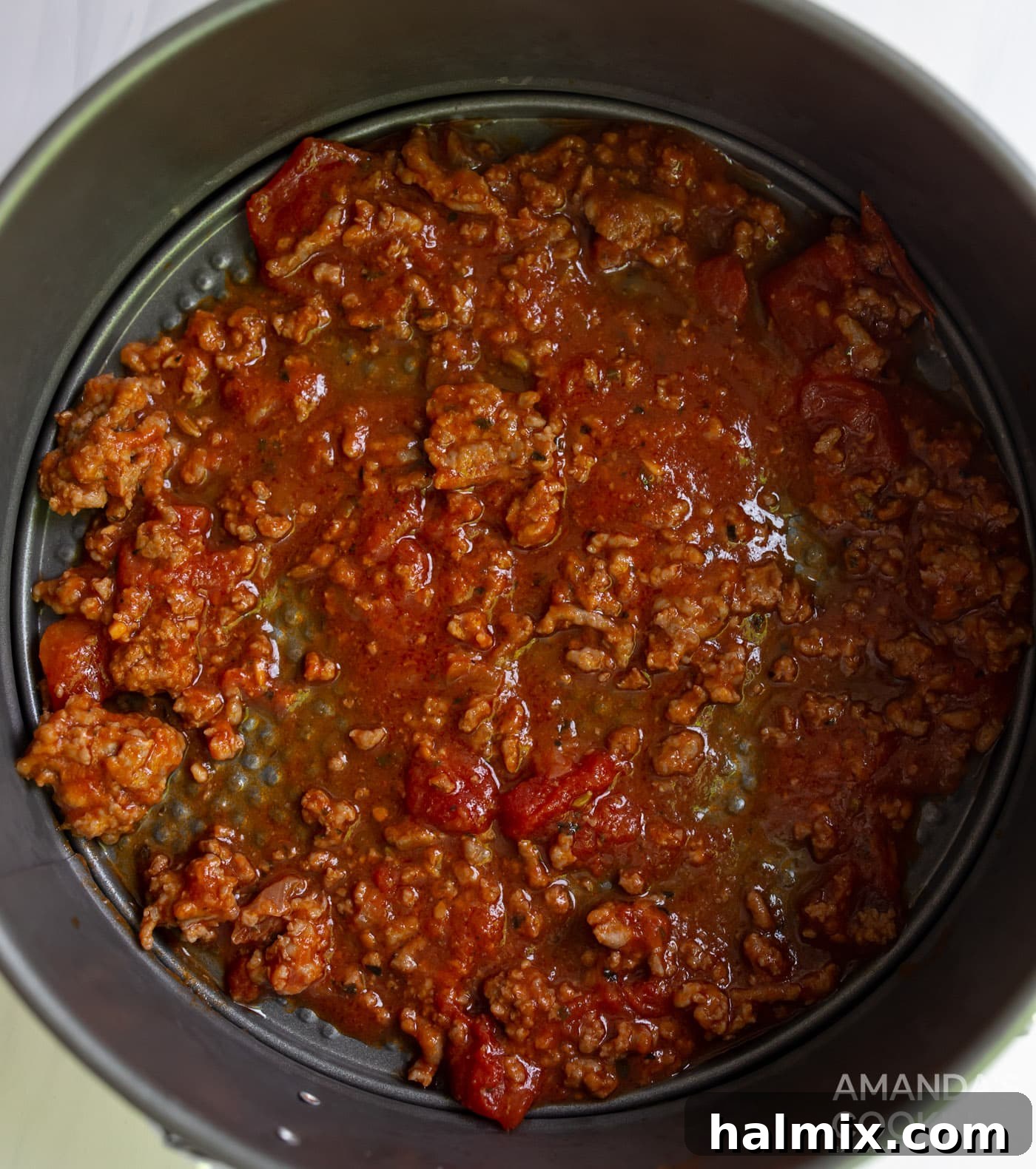Effortless Instant Pot Lasagna 8 A generous layer of rich meat sauce spread at the bottom of an 8-inch springform pan, creating the base for the lasagna.
