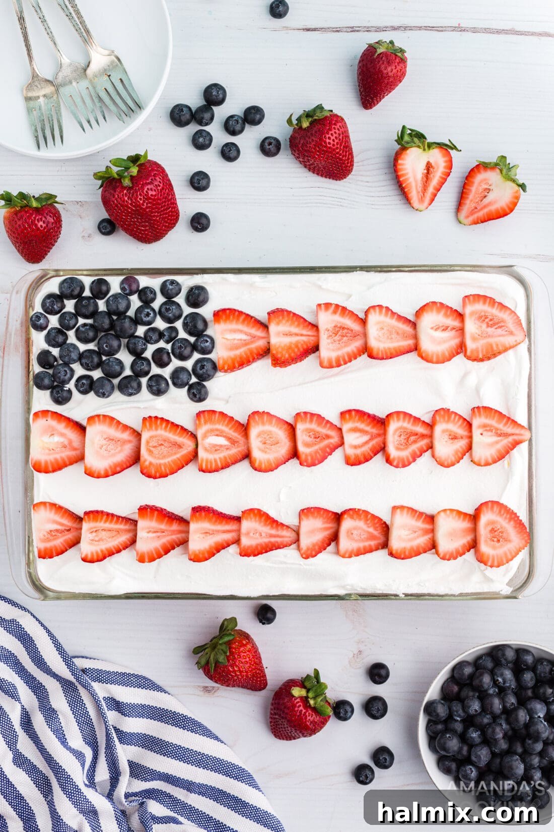 American flag decorated poke cake, vibrant with red strawberries and blue blueberries on a white whipped topping.