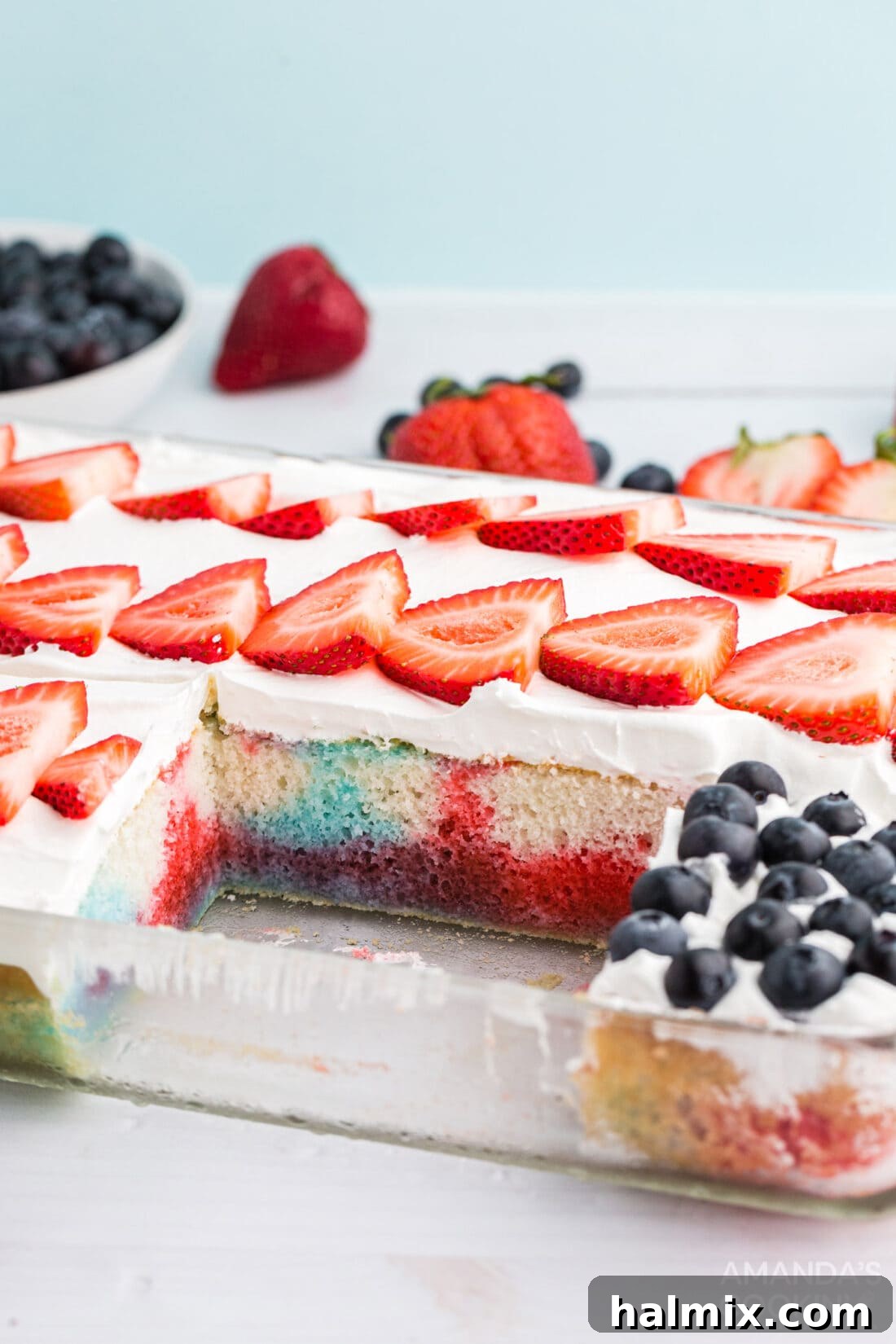 A Red, White, and Blue Poke Cake with one slice removed, showcasing the flag design and the Jell-O infused interior.