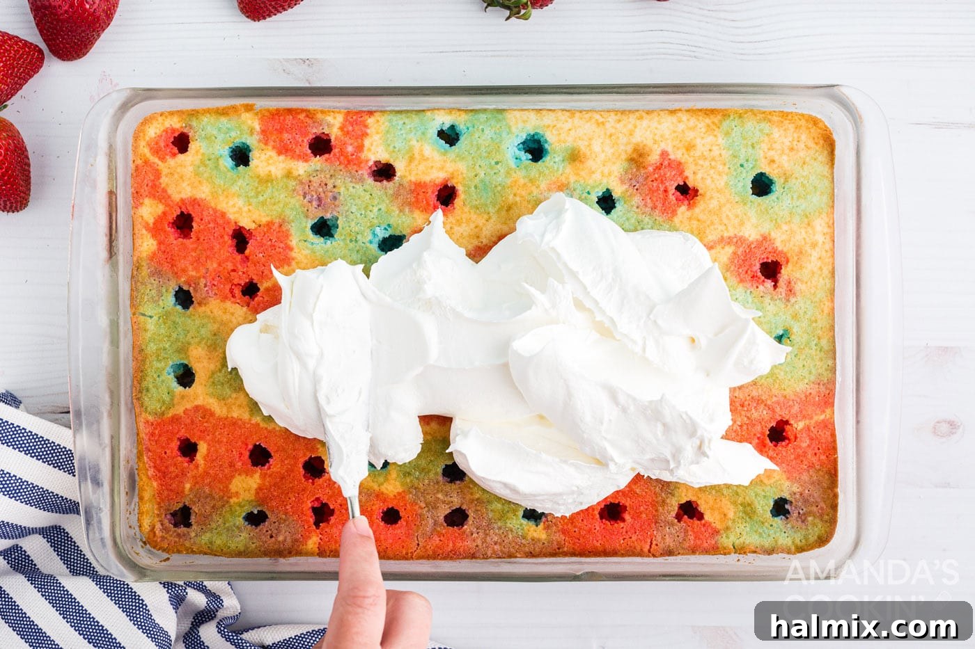 Cool Whip being spread smoothly over the top of a poke cake, covering the Jell-O infused surface.