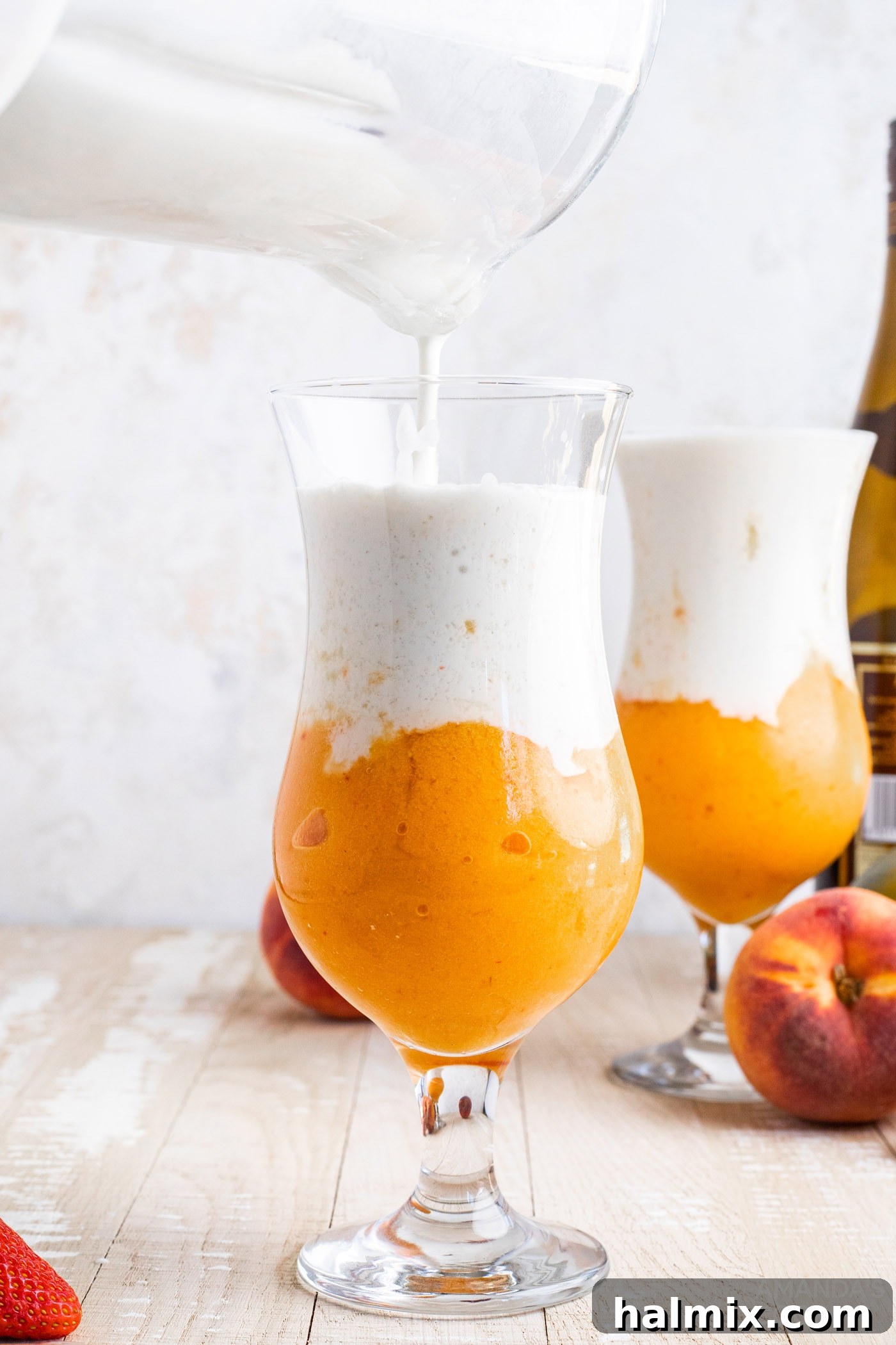 Pouring coconut cream slush into fruit slush in a glass, creating a layered effect