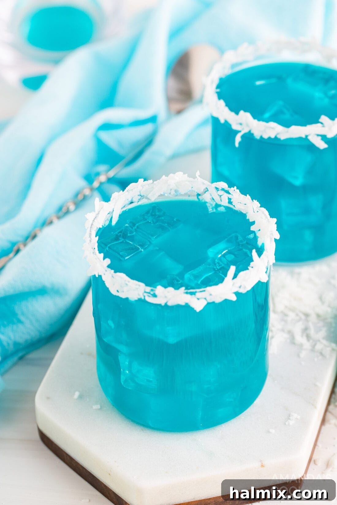 Neptune's Kiss Cocktail 2 Ocean Water Cocktail in elegant glasses with tropical garnishes, sparkling with ice and blue hues.