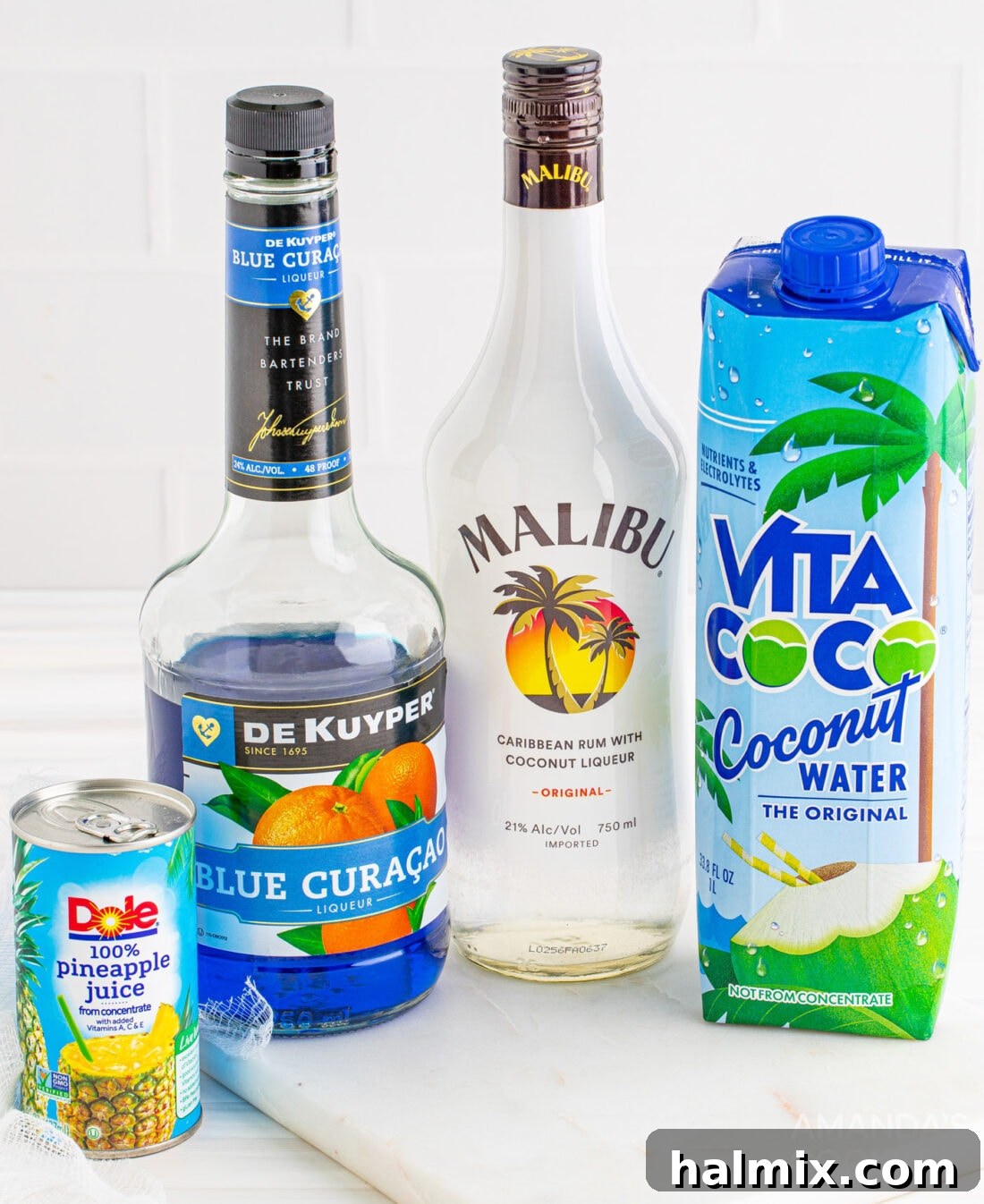 Neptune's Kiss Cocktail 4 Arrangement of ingredients for an Ocean Water Cocktail: bottles of blue curacao and coconut rum, fresh pineapple, and coconut water.