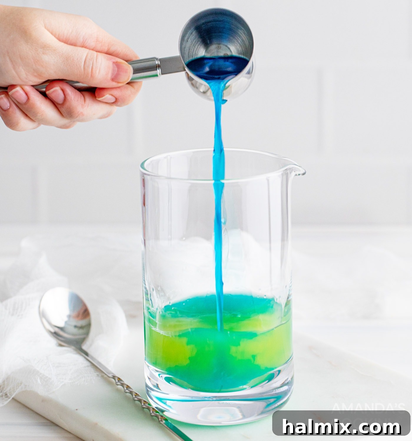 Neptune's Kiss Cocktail 6 Pouring vibrant blue curacao into a cocktail mixing glass with other ingredients for the Ocean Water Cocktail.