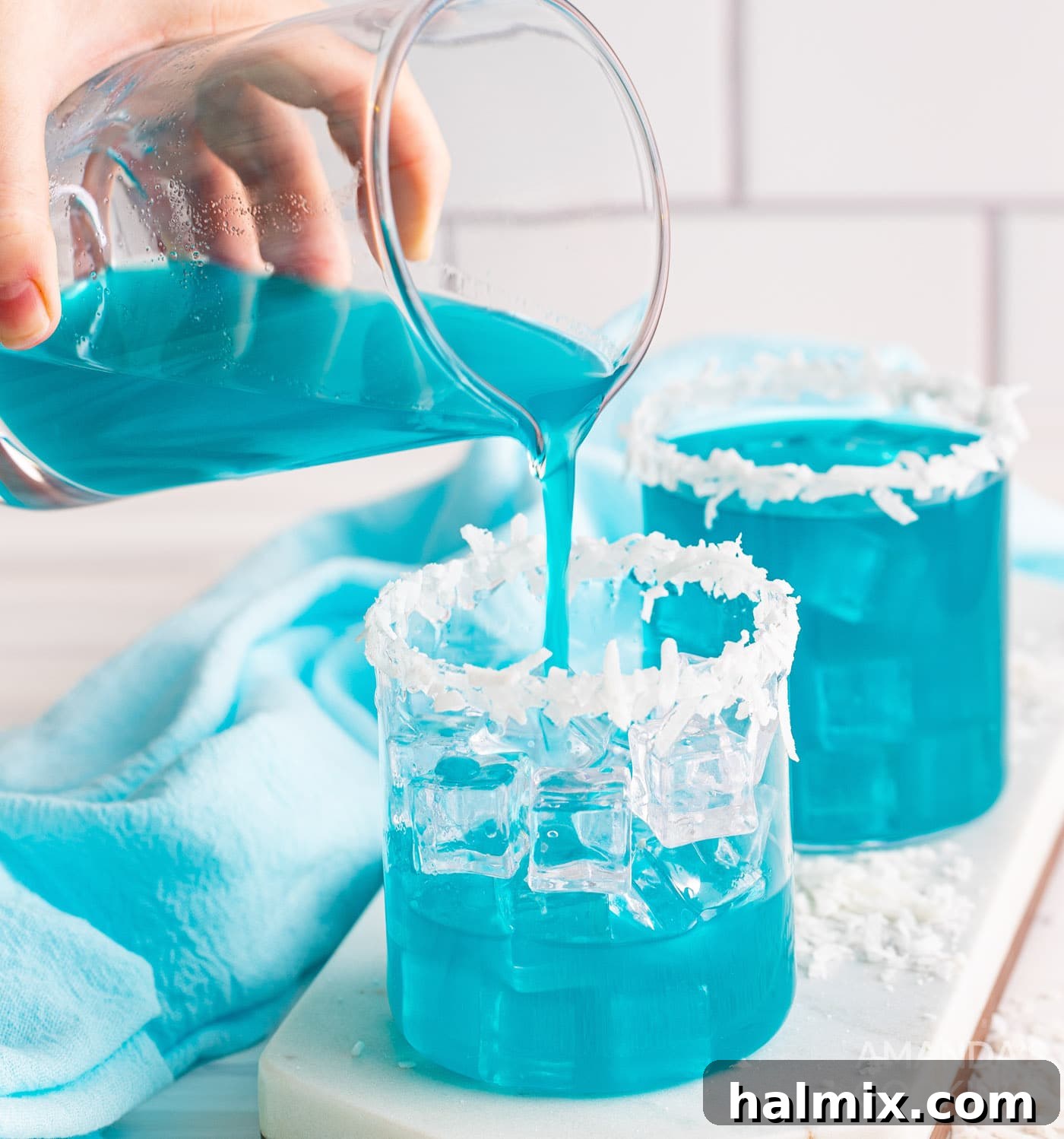 Neptune's Kiss Cocktail 8 Pouring a perfectly mixed Ocean Water Cocktail into a glass filled with ice and a coconut rim.
