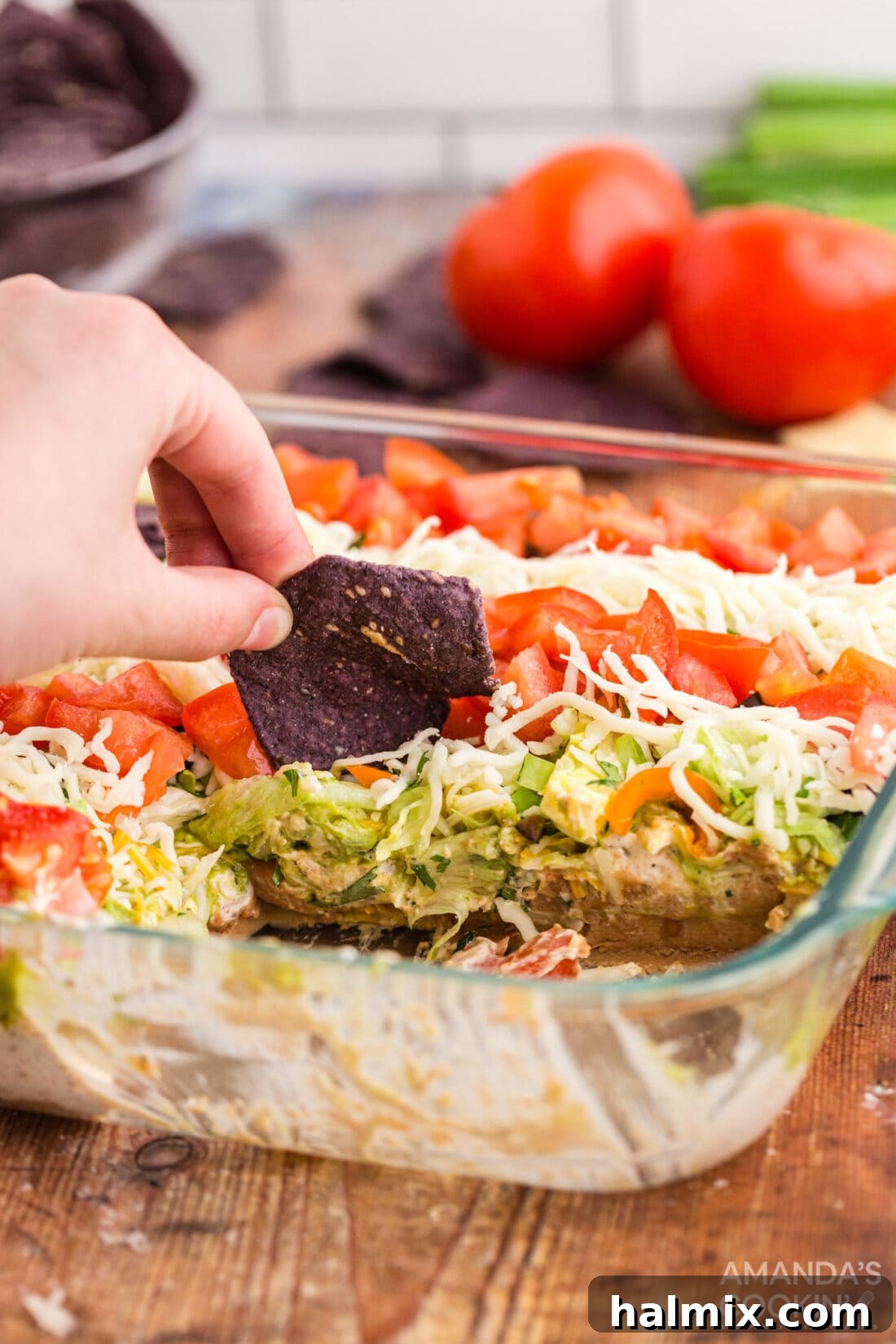 Hand scooping taco salad with a tortilla chip, showing the layers.
