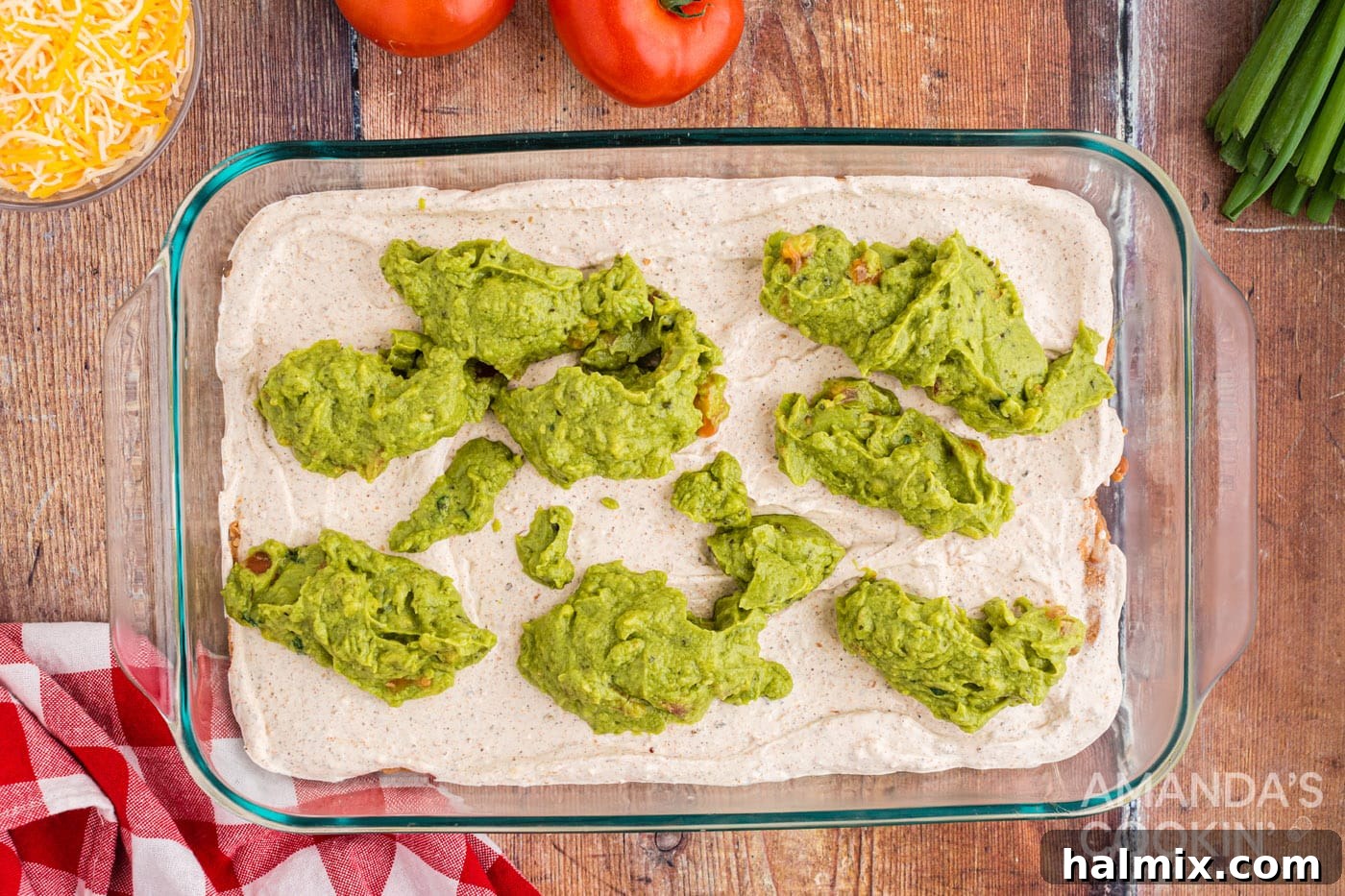 Dollops of guacamole being spread over the cream cheese layer in the dish.