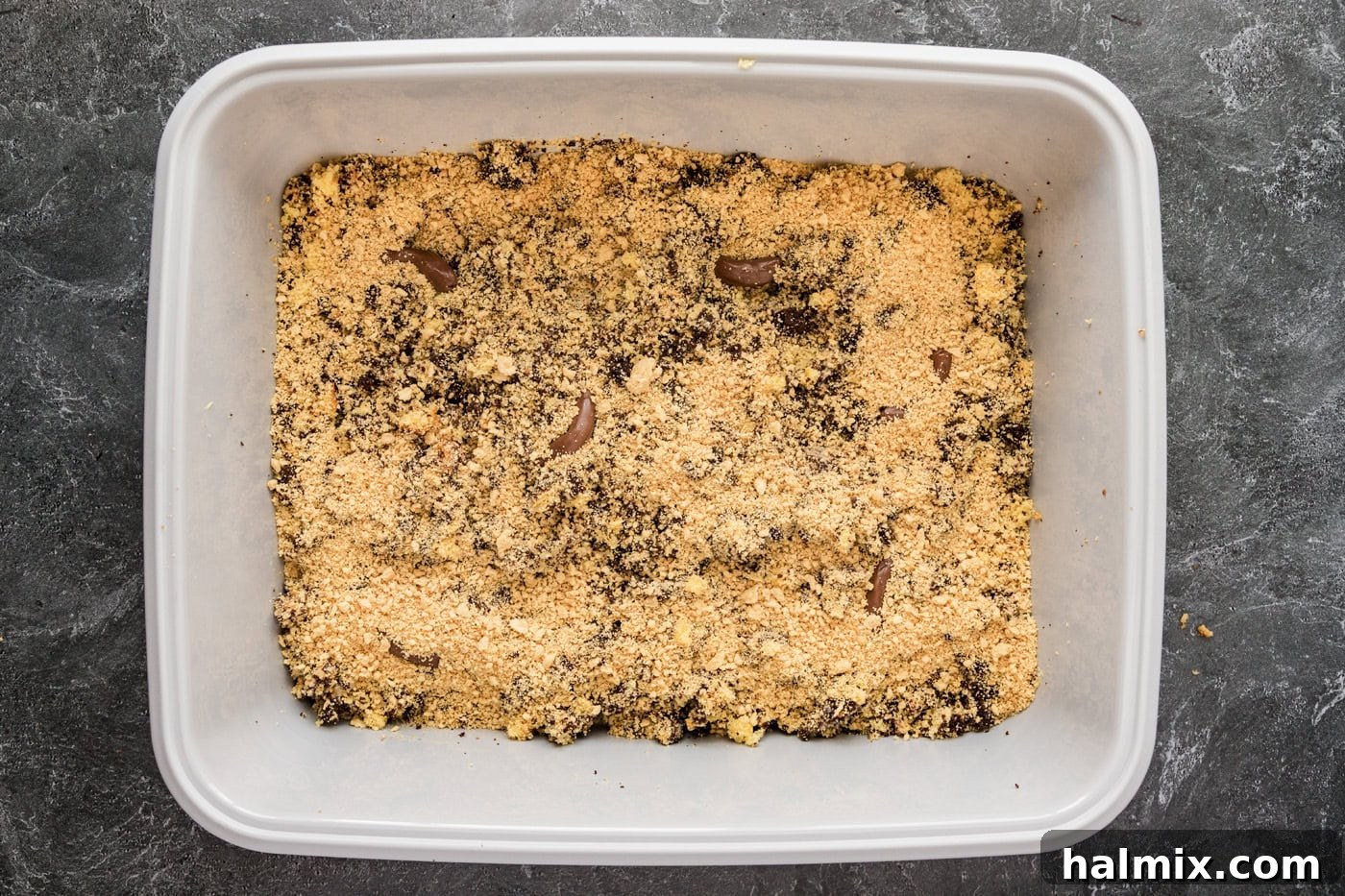 More crushed cookies are added over the cake mixture, preparing the ground for the final realistic touches.