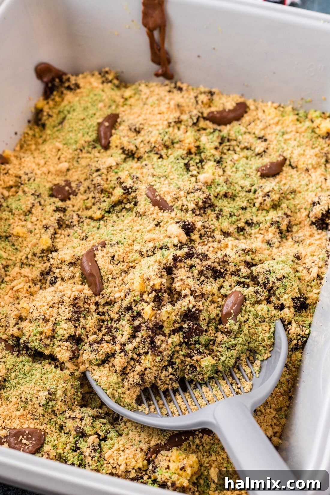 A close-up view of a litter scoop digging into a Kitty Litter Cake, showing the crumbly texture and chocolate 'surprises'.