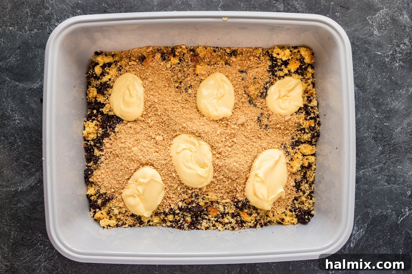 Chilled pudding being added on top of crumbled cake and crushed Oreos in a new litter box.