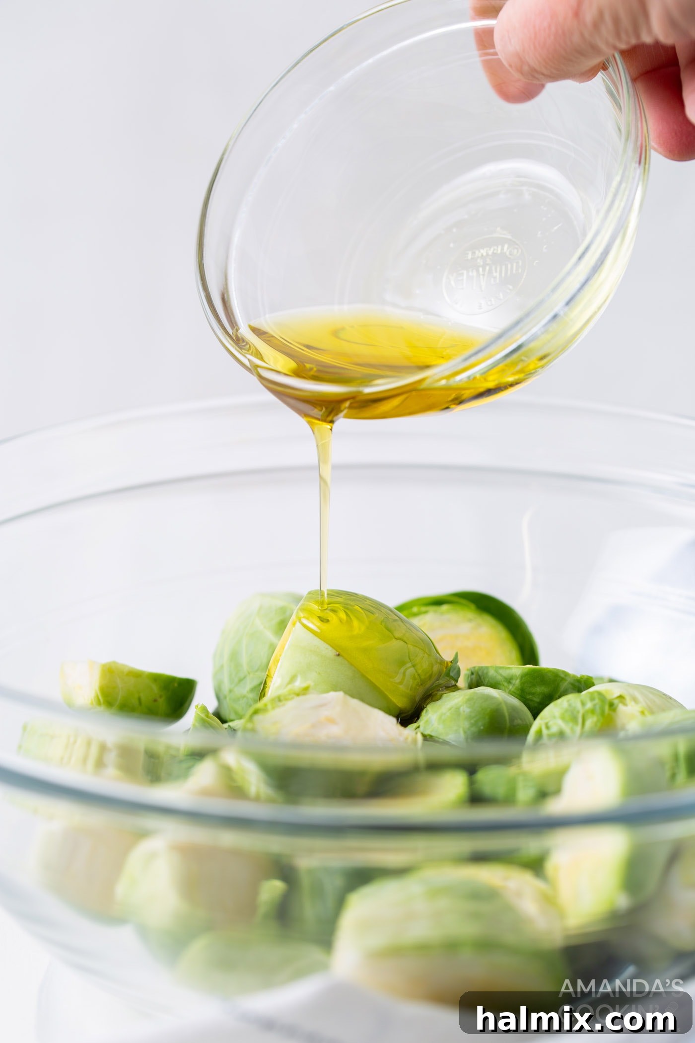 Pouring olive oil over halved Brussels sprouts in a mixing bowl.
