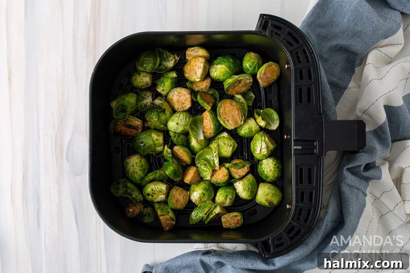 Halved Brussels sprouts spread out evenly in an air fryer basket, ready for cooking.