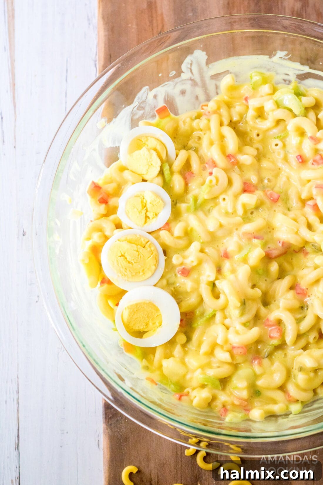 A bowl of creamy Amish Macaroni Salad, garnished with slices of hard-boiled eggs and a sprinkle of paprika, invitingly presented on a rustic wooden surface, perfect for sharing at a potluck or picnic.