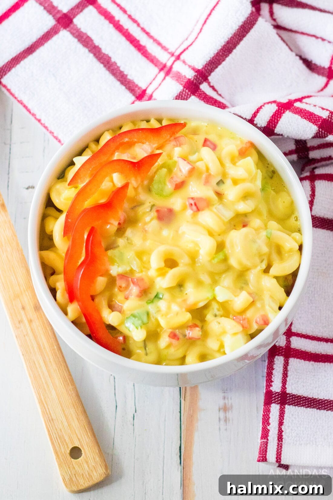 A close-up view of a small ceramic bowl filled with creamy Amish Macaroni Salad, garnished with finely diced red bell pepper for a pop of color and freshness, ready to be served.