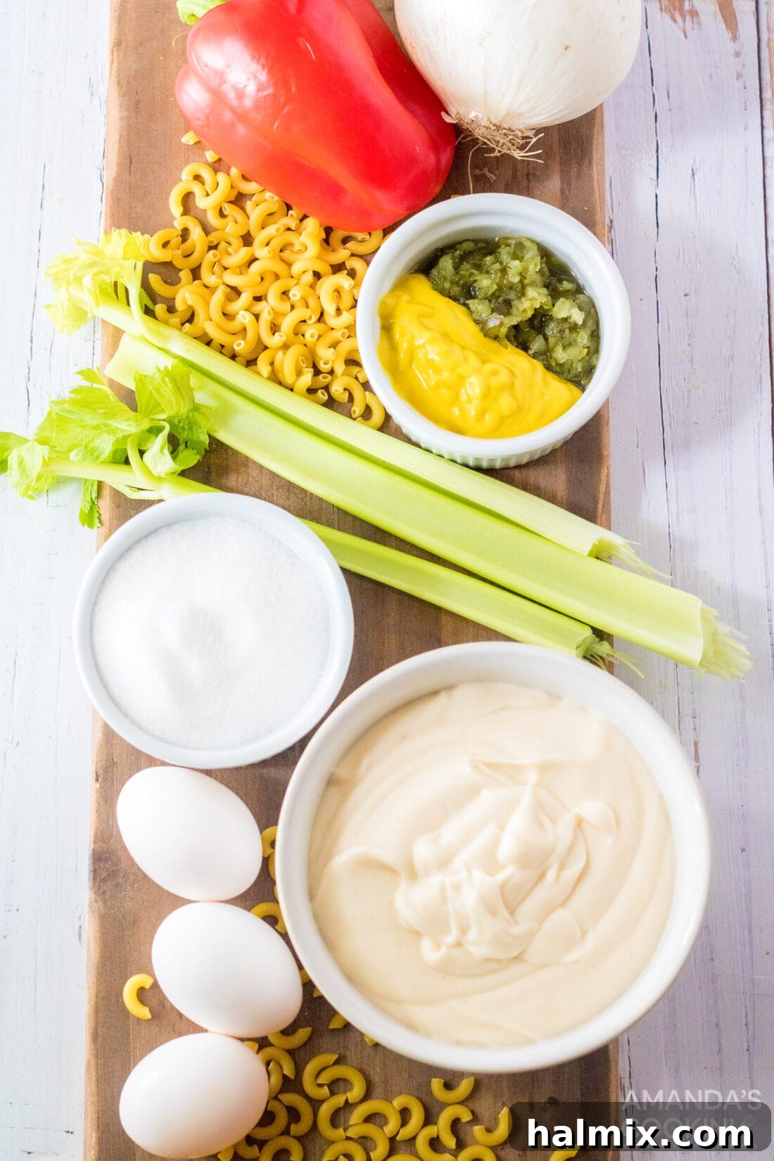 A vibrant flat lay of all the fresh ingredients required to make a delicious Amish Macaroni Salad, including cooked elbow macaroni, hard-boiled eggs, chopped bell pepper, celery, onion, and a bowl of creamy dressing, set on a clean kitchen counter.