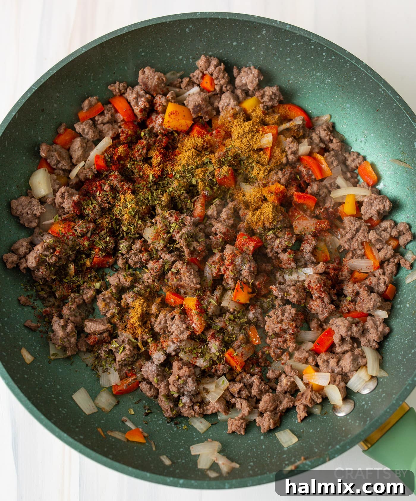 Ground beef, diced peppers, garlic, seasonings, and onions cooking together in a skillet.