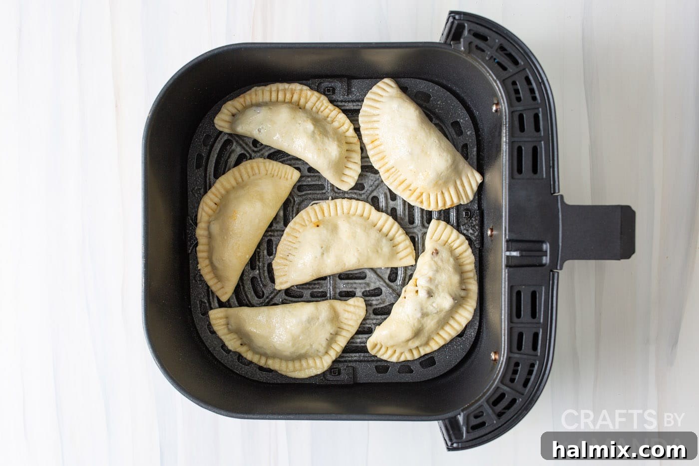 Empanadas arranged in a single layer inside an air fryer basket, ready for cooking.