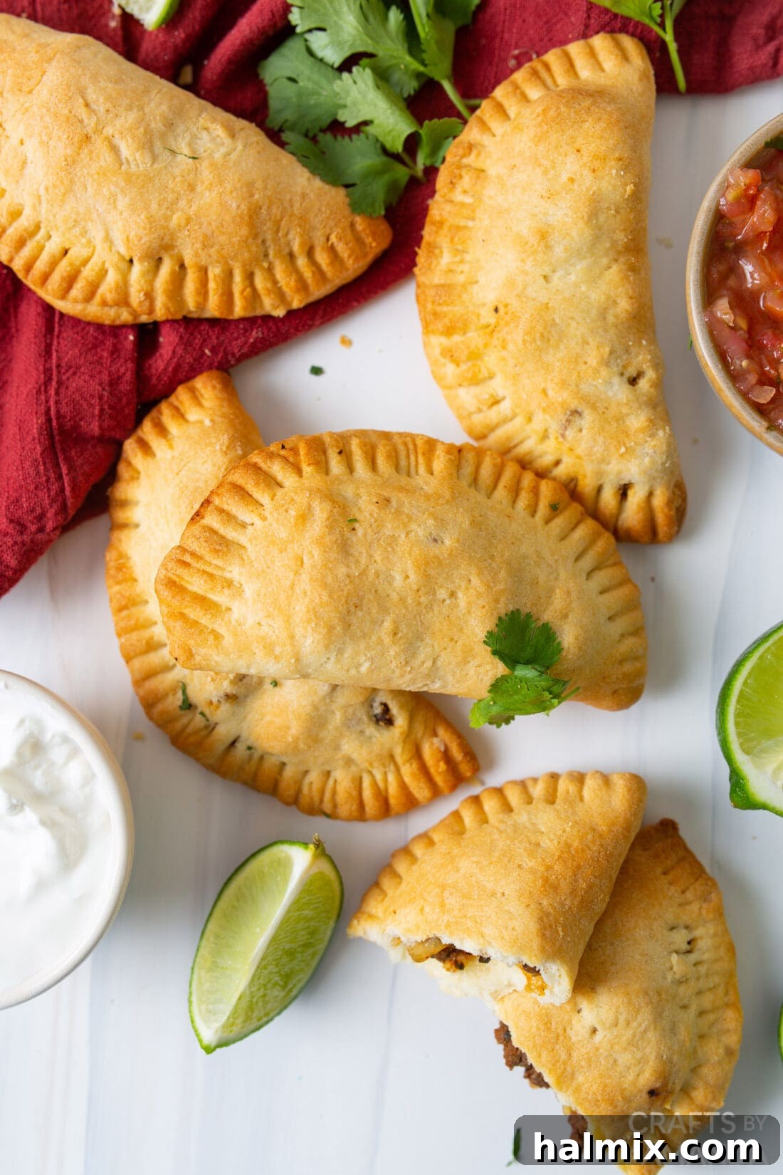 Overhead photo of a platter of golden brown beef empanadas, some with dipping sauce.