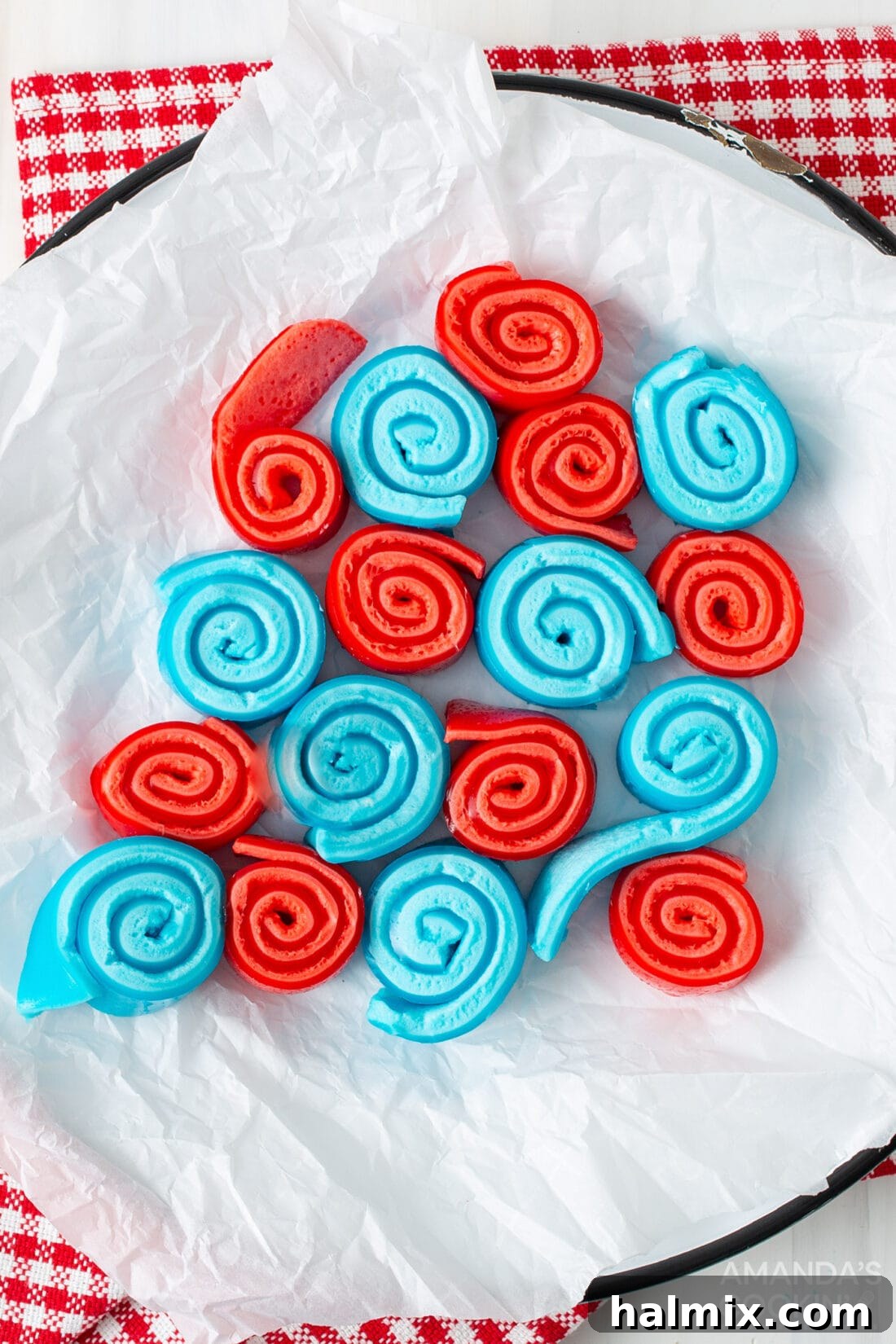 Two plates of colorful Jello Roll Ups, one with red and blue, the other with various colors. The red and blue roll ups are arranged neatly on a white plate, showcasing their vibrant layers.