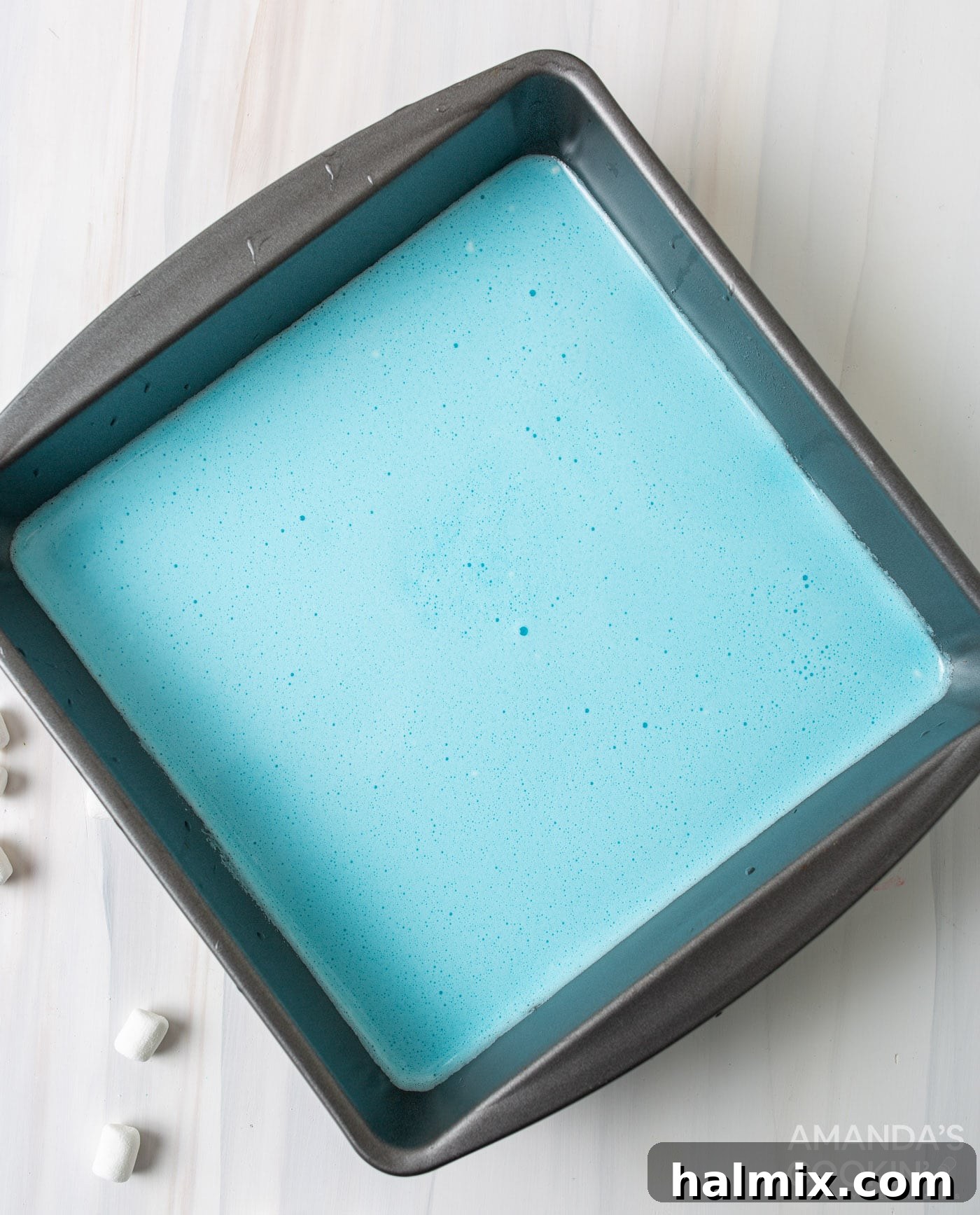 A close-up shot of the blue jello and marshmallow mixture in a glass bowl, showcasing its smooth texture and vibrant color.
