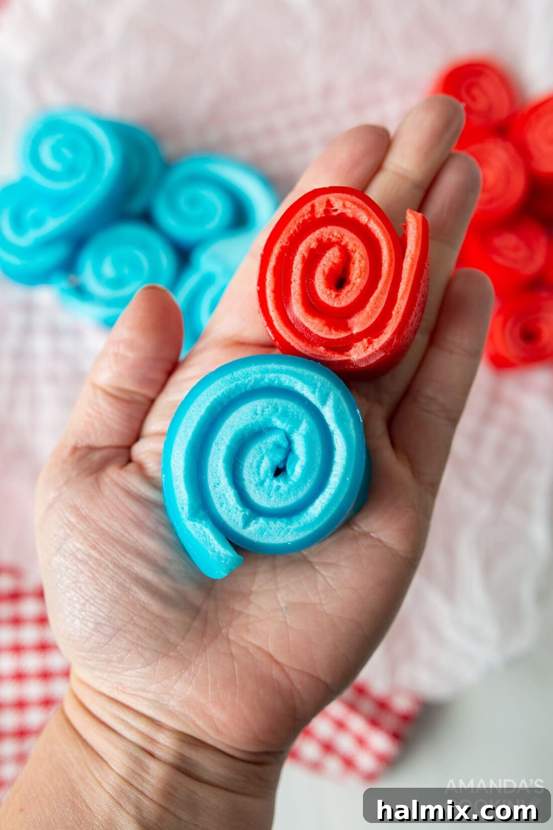 A hand holding a perfectly formed red and blue Jello Roll Up, showcasing its vibrant layers and inviting texture.
