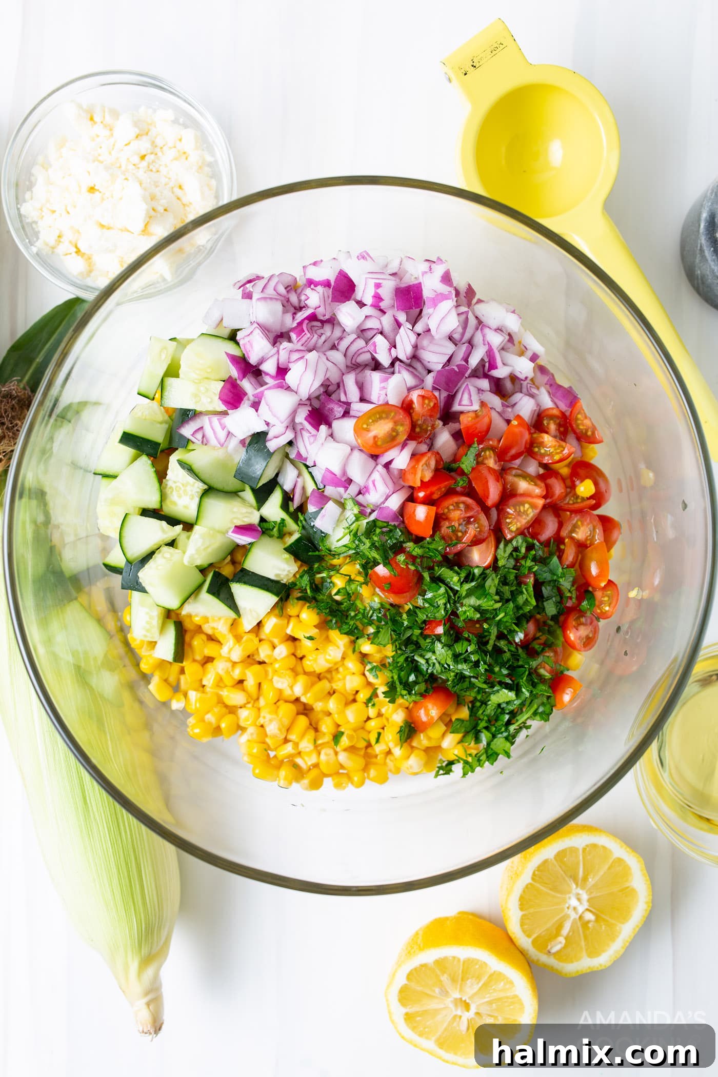 A mixing bowl filled with freshly cut corn kernels, halved cherry tomatoes, finely chopped red onion, diced cucumber, and minced fresh basil, ready for tossing.