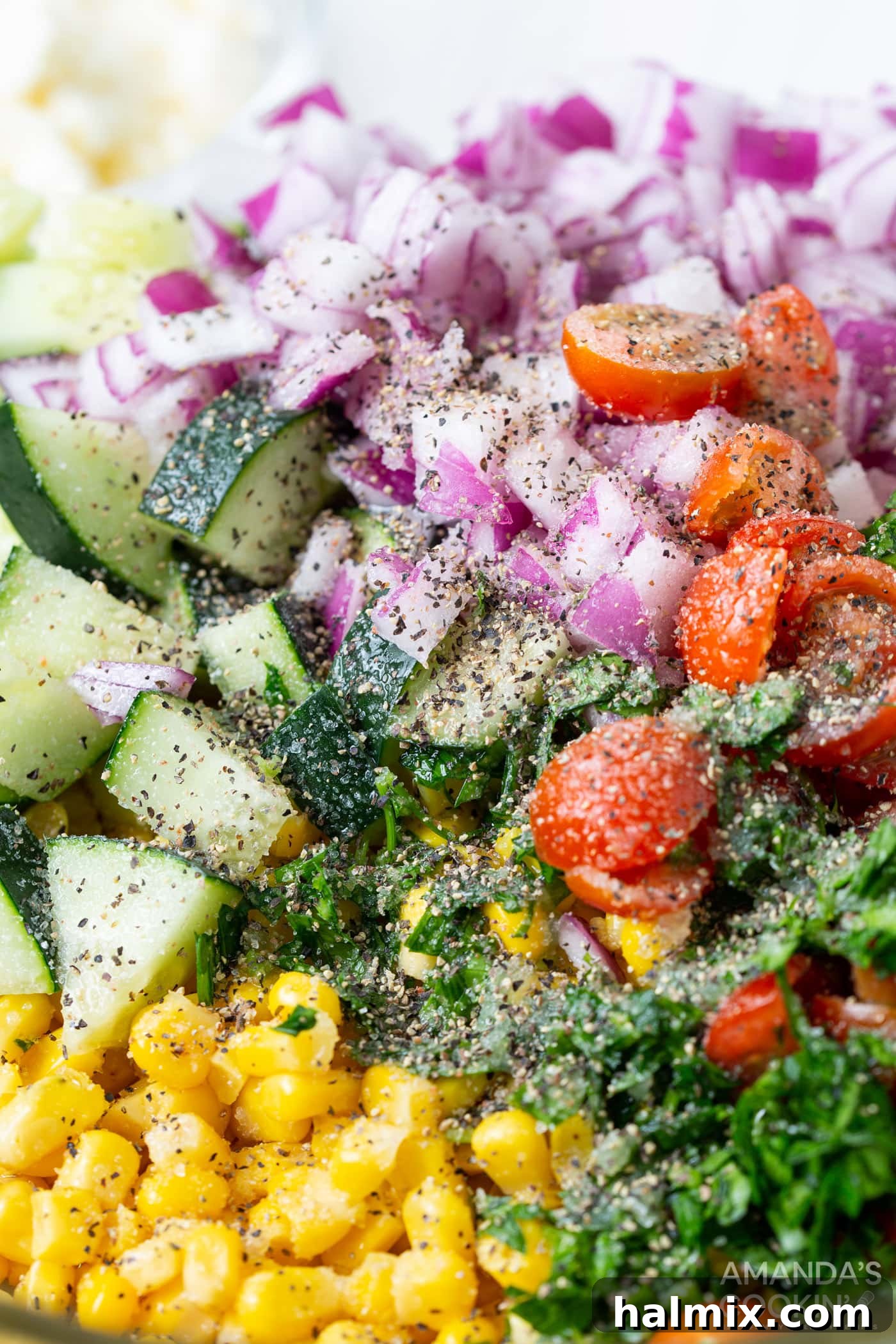Close-up of corn salad ingredients in a bowl, showing a sprinkle of freshly ground black pepper and salt over the colorful mix of corn, tomatoes, and herbs, before final tossing.