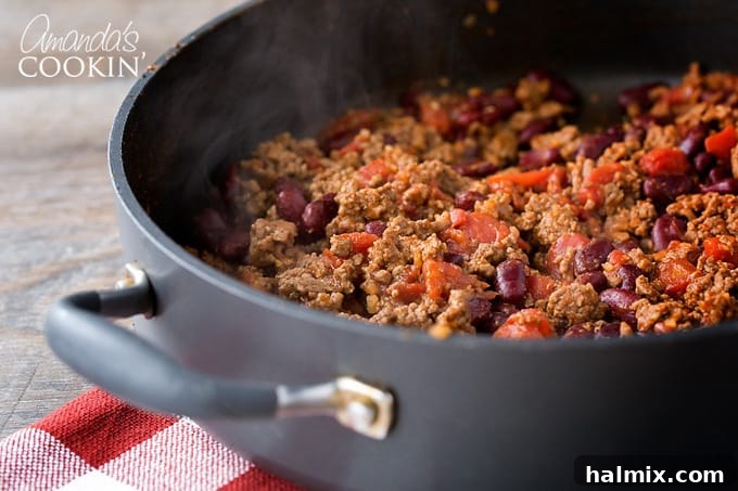 Chili Mac is a delicious combination of ground beef, beans, tomatoes, chili seasoning, and macaroni. This chili mac recipe makes a hearty dinner or a delicious cup of warmth for friends watching football! #chilimac #chili #groundbeef #beans #macaroni #footballrecipes #comfortfood #winterfood #chili Visual guide showing how to brown ground beef in a skillet, drain excess fat, and then add chili seasoning, water, beans, and diced tomatoes, stirring them all together.