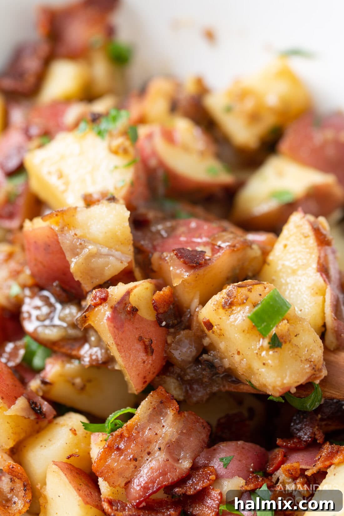 Tangy Bacon Potato Salad 3 A close-up view of warm German Potato Salad, showcasing its tender red potatoes, diced purple onions, and crispy bacon pieces, glistening with its signature vinegar dressing.