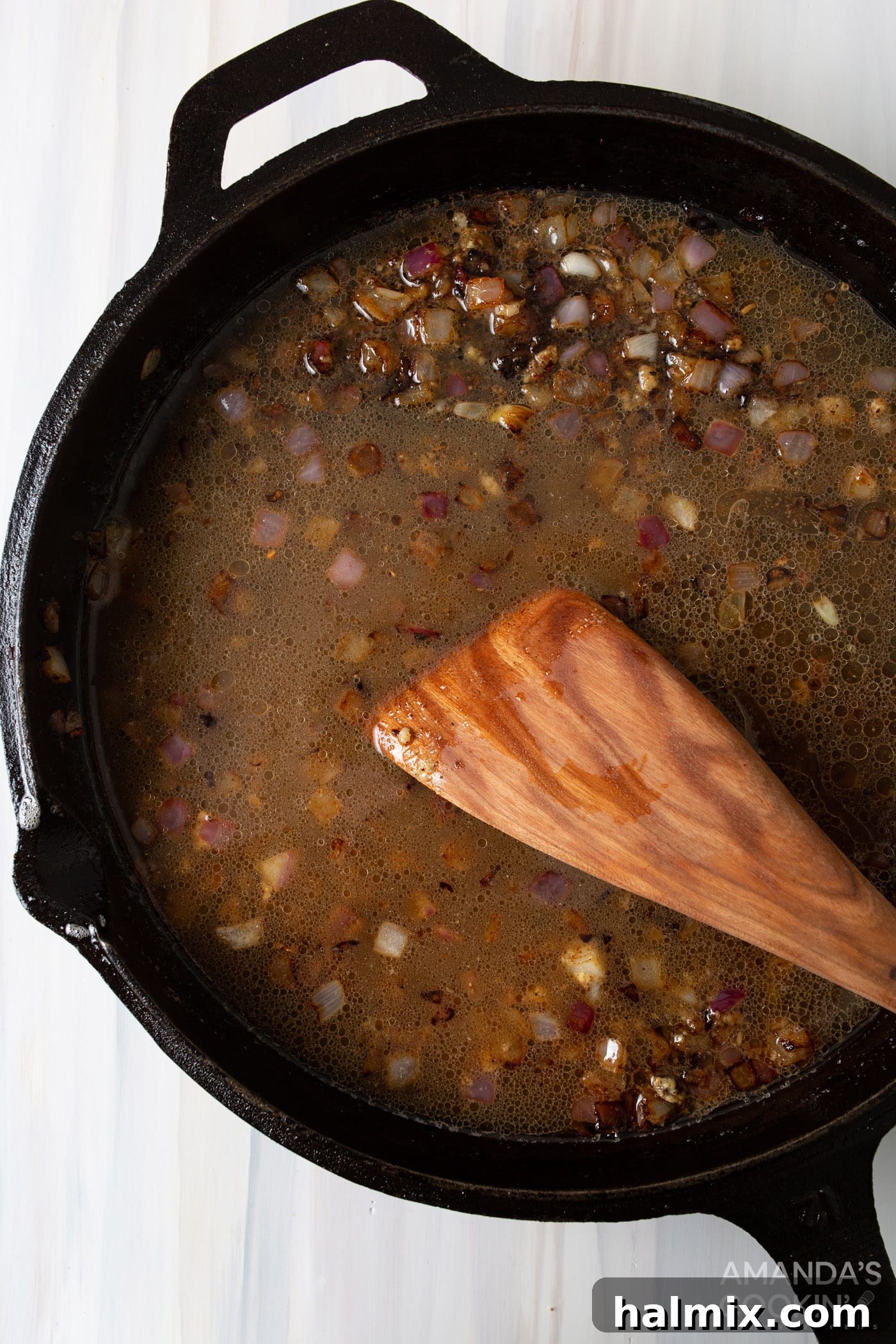 Tangy Bacon Potato Salad 5 A wooden spatula gently stirring minced garlic and purple onion in a hot skillet, preparing the flavorful base for the German potato salad dressing.