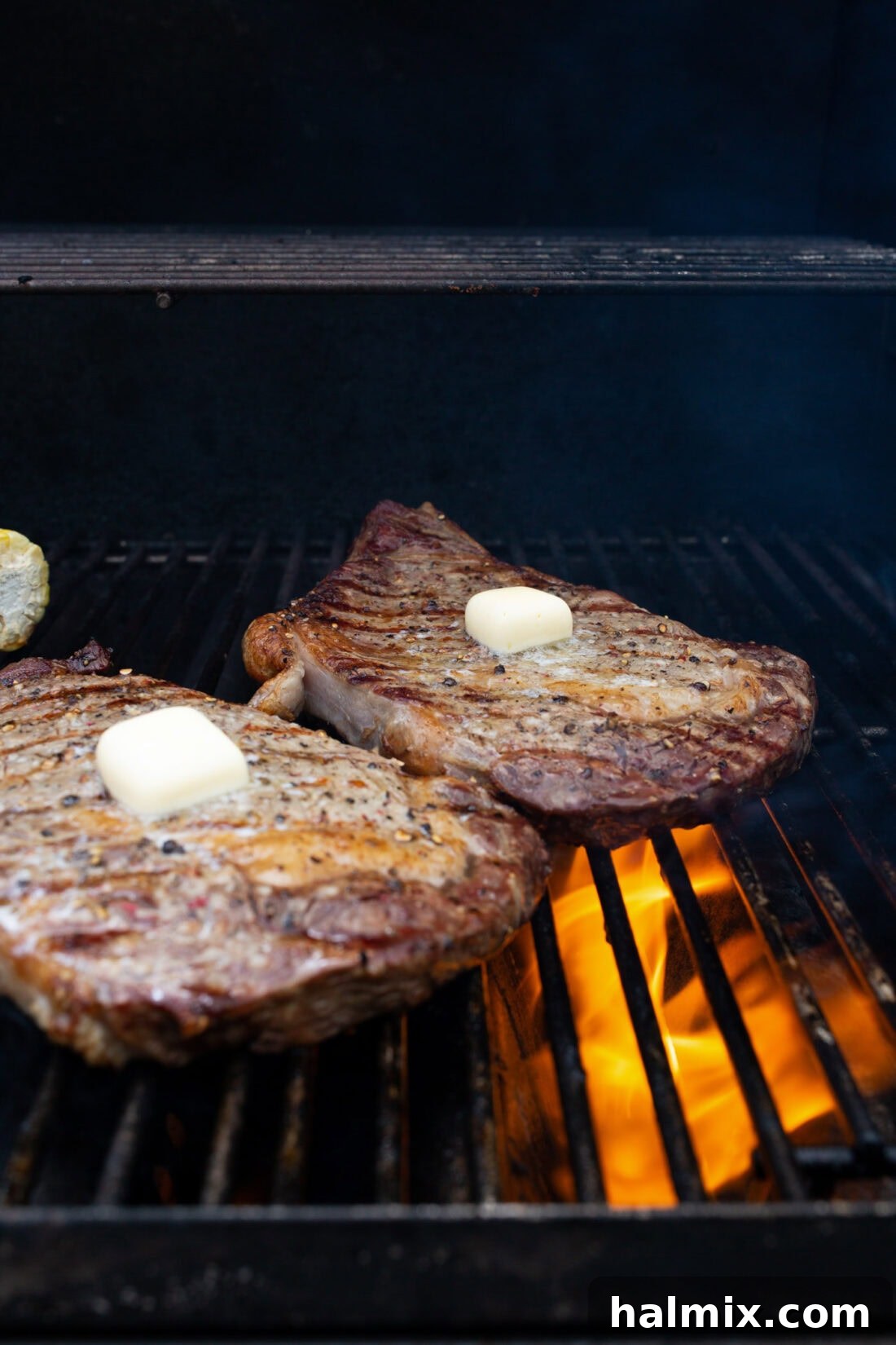 Two prime steaks sizzling on a hot grill, with generous pats of butter melting on top, enhancing flavor and juiciness