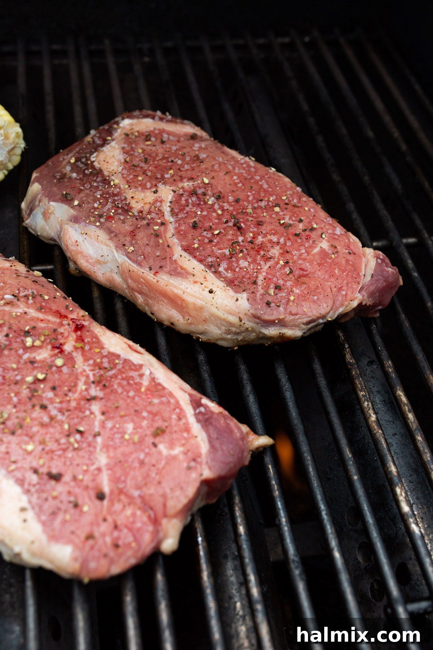 Two New York strip steaks searing perfectly on a very hot grill, forming a delicious crust