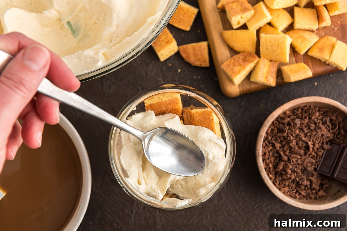A spoon adding a creamy layer of Bailey's mascarpone cheese mixture over the ladyfingers in a parfait dish.