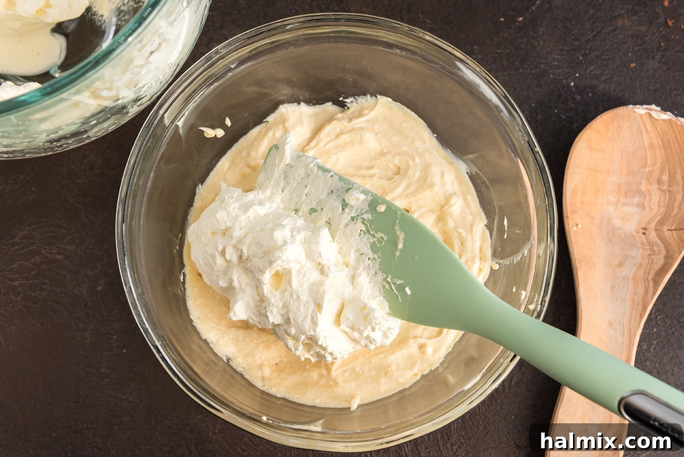 A spatula gently folding the beaten whipped cream into the luscious Bailey's-infused mascarpone mixture.