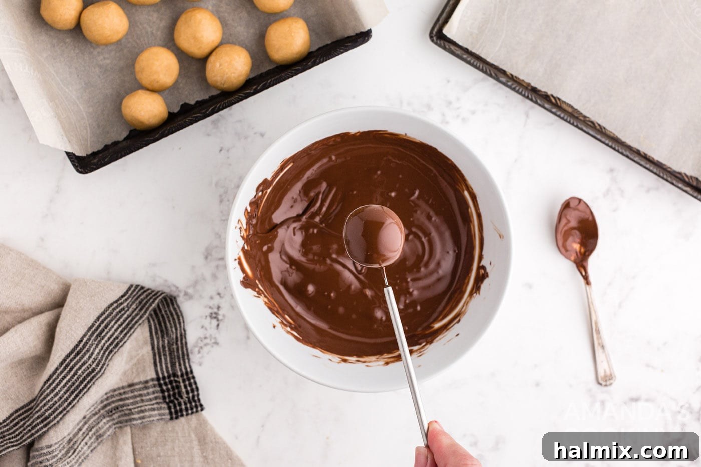 A chocolate-coated peanut butter ball resting on a dipping tool, showcasing its freshly applied chocolate shell.