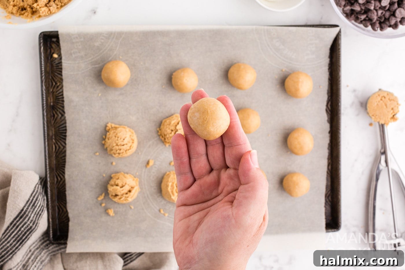 A hand shaping a scooped portion of peanut butter mixture into a smooth, round ball.