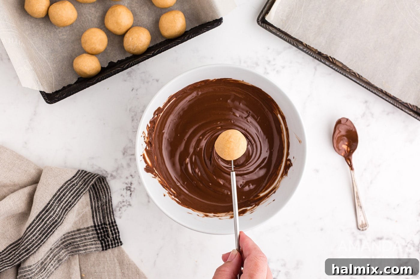 A peanut butter ball being carefully dipped into a bowl of melted chocolate.