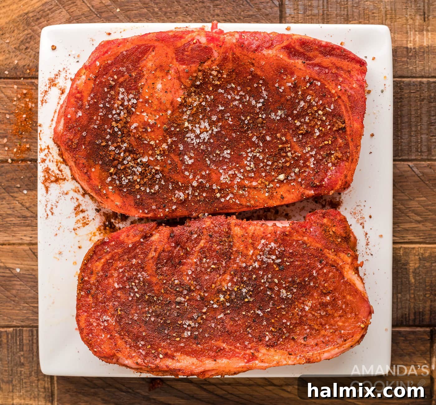 Seasoned ribeye steaks on a cutting board, ready for the smoker.