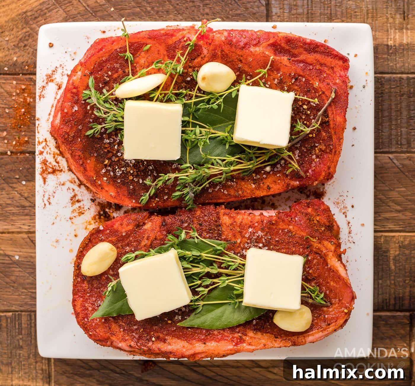 Ribeye steaks topped with pats of butter, bay leaves, and fresh thyme sprigs.