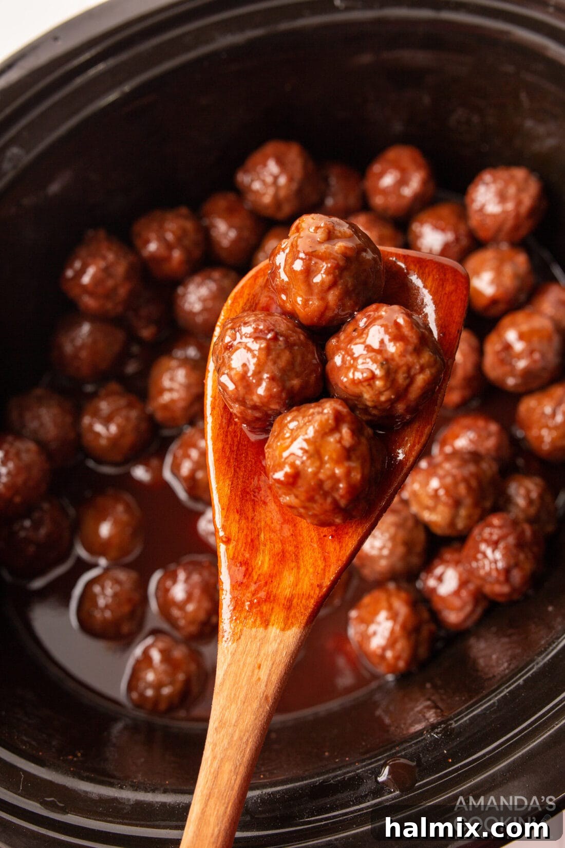 Tender, glossy grape jelly meatballs being lifted from a slow cooker with a wooden spoon, ready to be served as an appetizer.