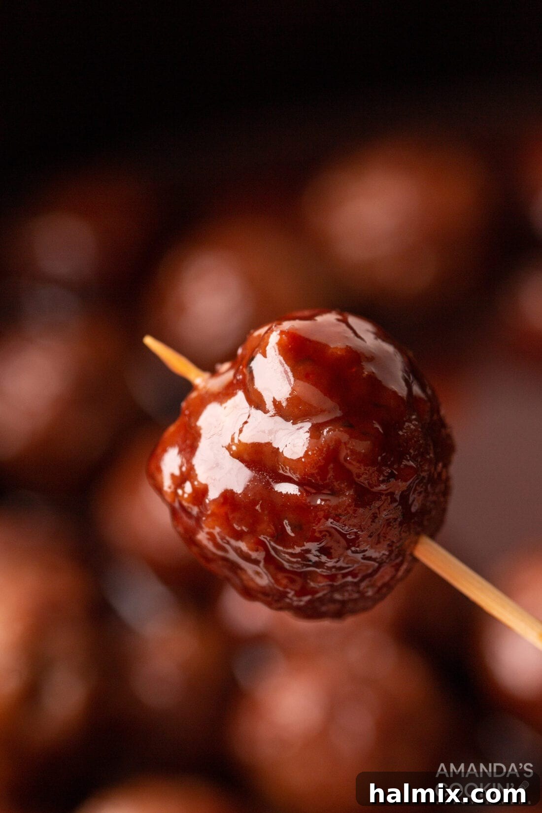 A single grape jelly meatball, perfectly coated in a glossy sauce, pierced with a toothpick and ready to be enjoyed as a delightful appetizer.