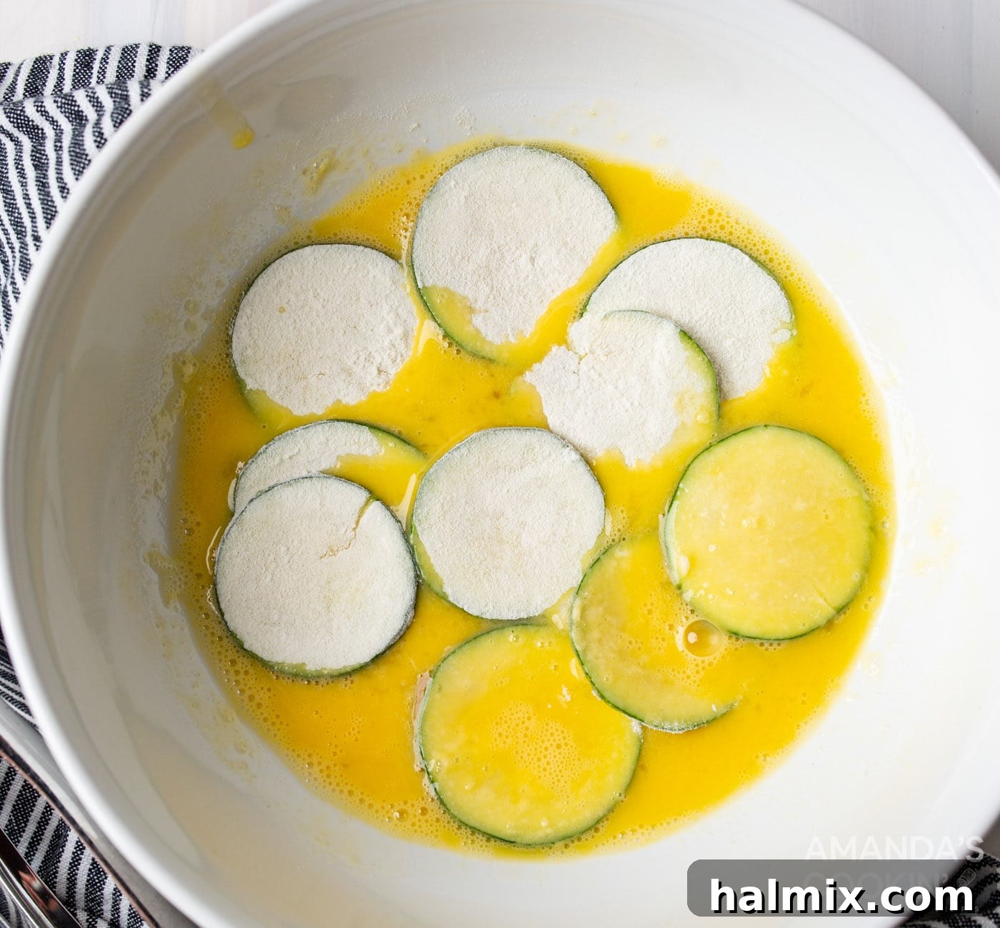 Dredging flour-coated zucchini slices in an egg wash