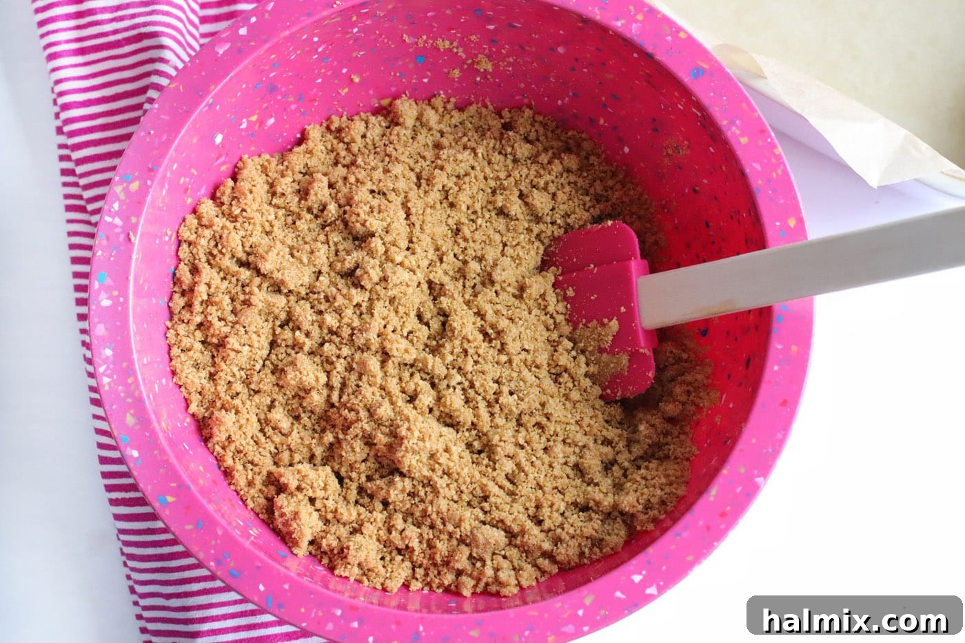 Graham cracker crumbs, melted butter, and water mixed in a bowl with a rubber spatula.